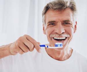Man smiling while preventing dental emergencies by brushing teeth